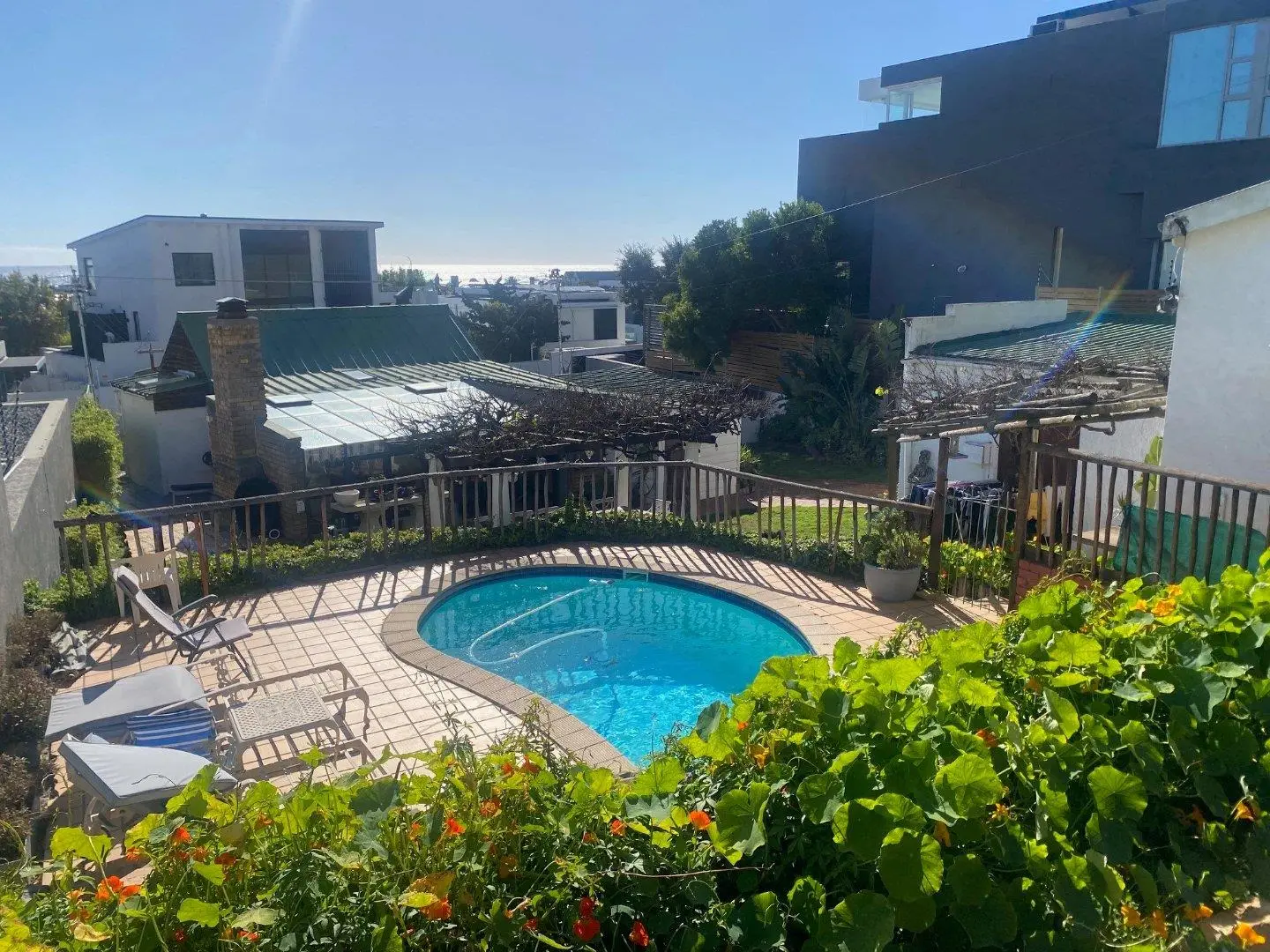 Small kidney-shaped pool in a terraced garden with flowers, and a view over rooftops towards the sea
