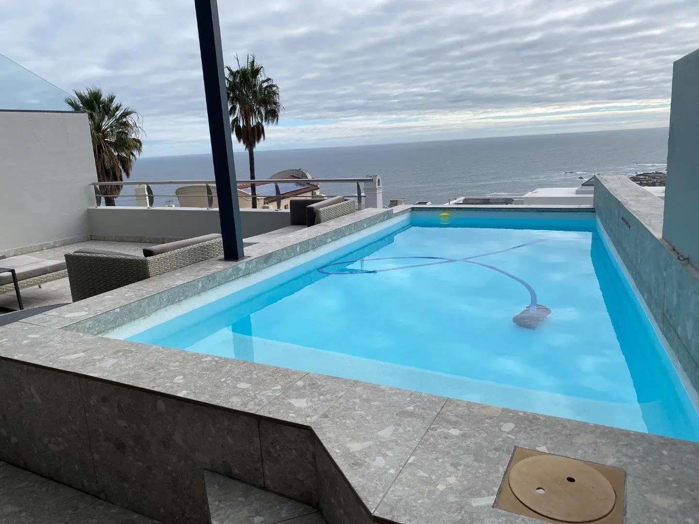 Rooftop swimming pool beside a terrace with the sea and a cloudy sky behind