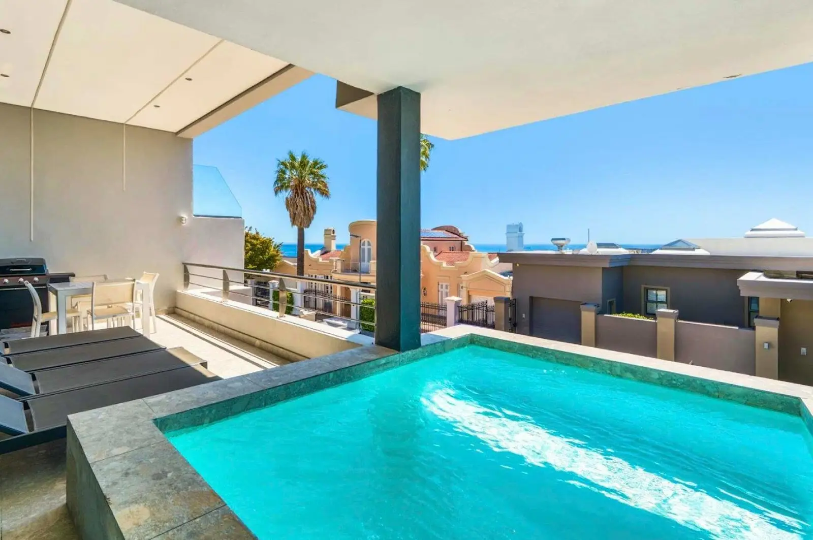 Plunge pool on a sunny balcony with palm trees and a glimpse of the sea beyond the neighbouring houses