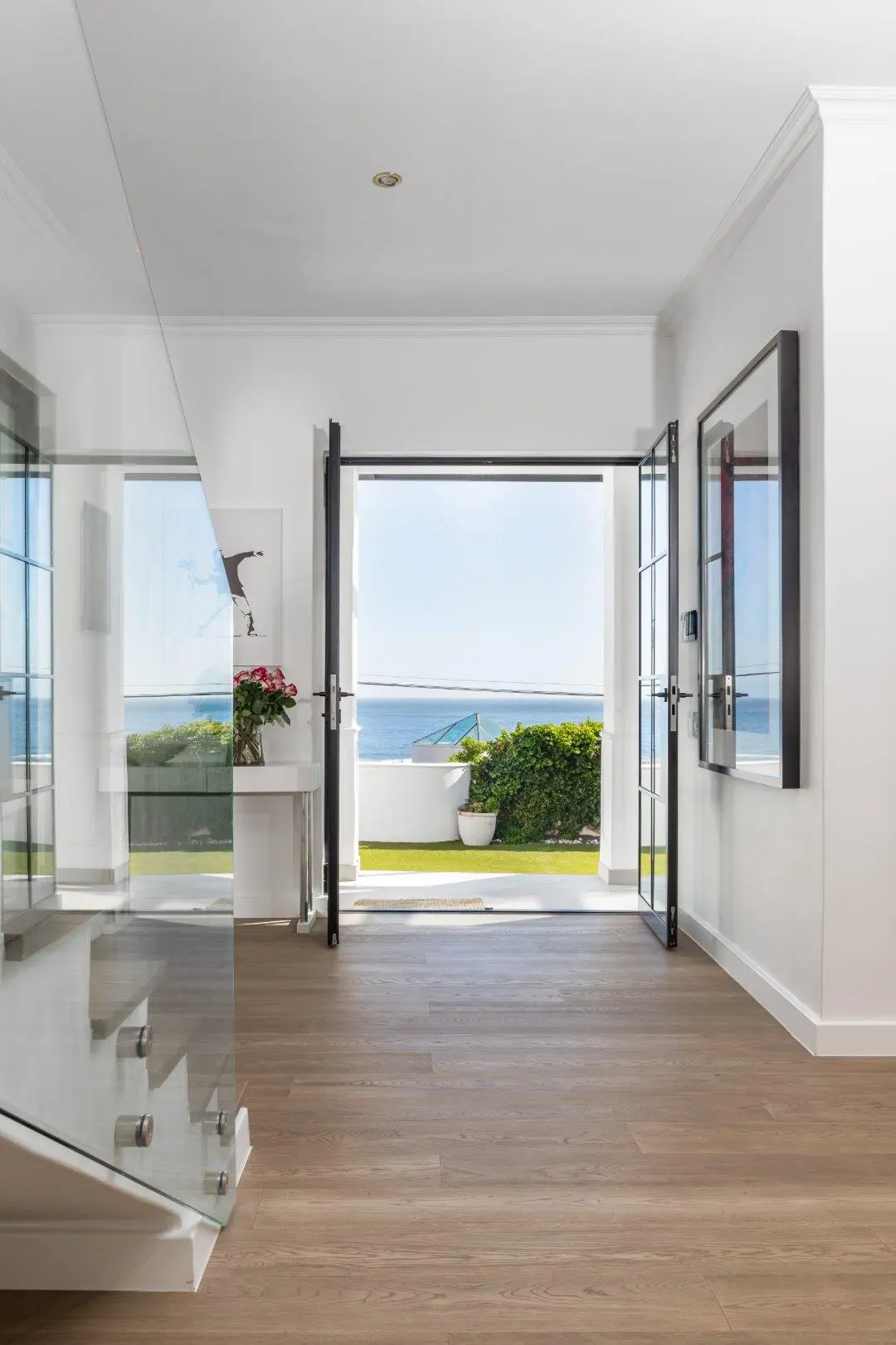 Hall looking out through open black-framed double doors to a lawn and the sea