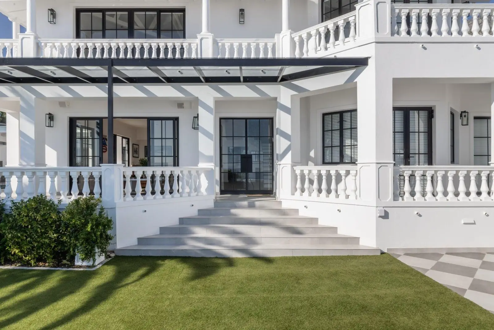 Front steps leading up to black-framed glass double doors under a balustraded balcony