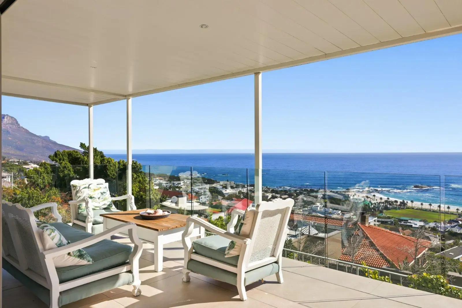 Covered terrace with armchairs and a glass balustrade, looking over Camps Bay to the sea